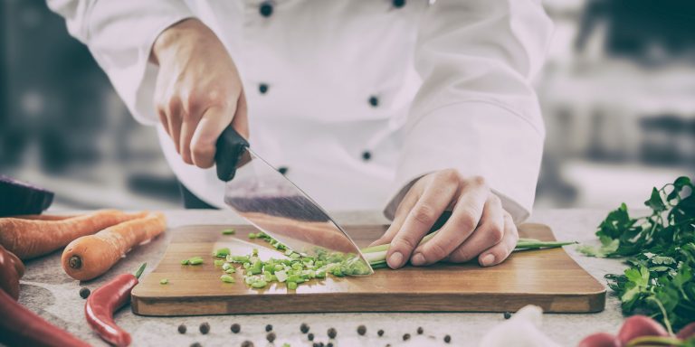 Chef in white jacket slicing green onions on a cutting board